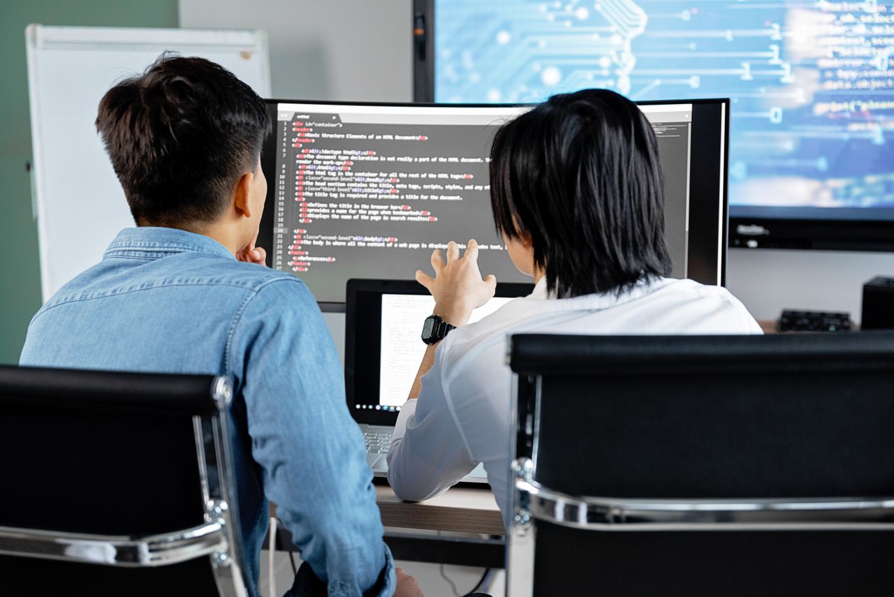 Offerings Two developers working together in an office, discussing code on a screen. Technology teamwork setting.